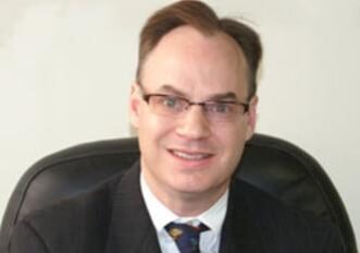 A man with glasses and a suit sitting in a chair.