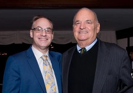 Two men standing next to each other in front of a curtain.